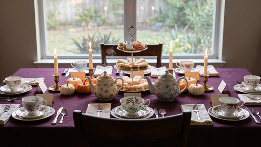 Halloween tea party table set with mismatched teacups, candles, and small pumpkins