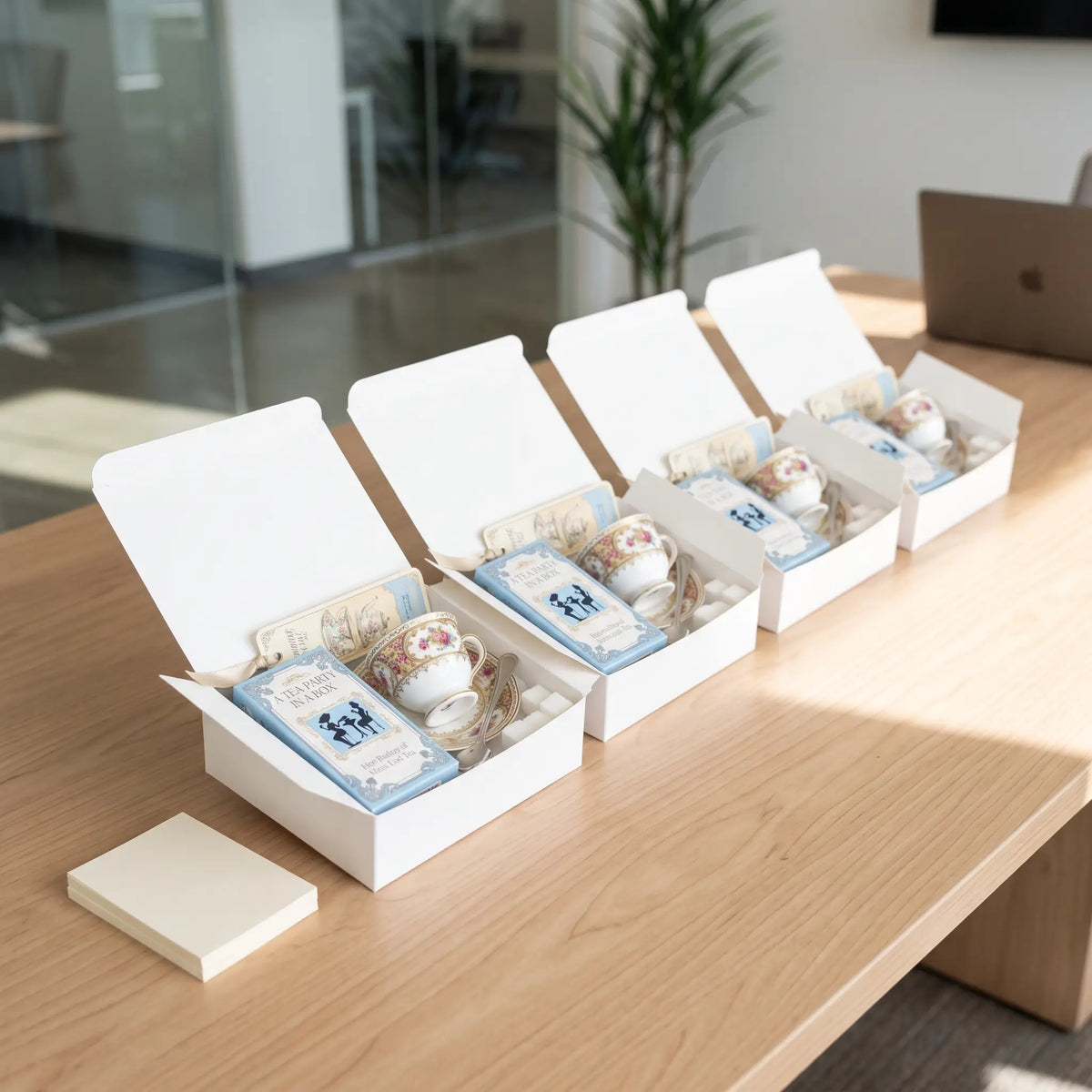 Corporate tea gifts: 4 Mini Tea Party In A Box gift sets with mini teacups lined up on an office conference table