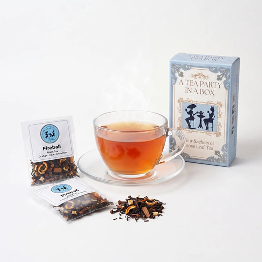 Fireball tea brewed in a clear glass teacup beside two labeled loose leaf tea sachets and the A Tea Party In A Box gift box