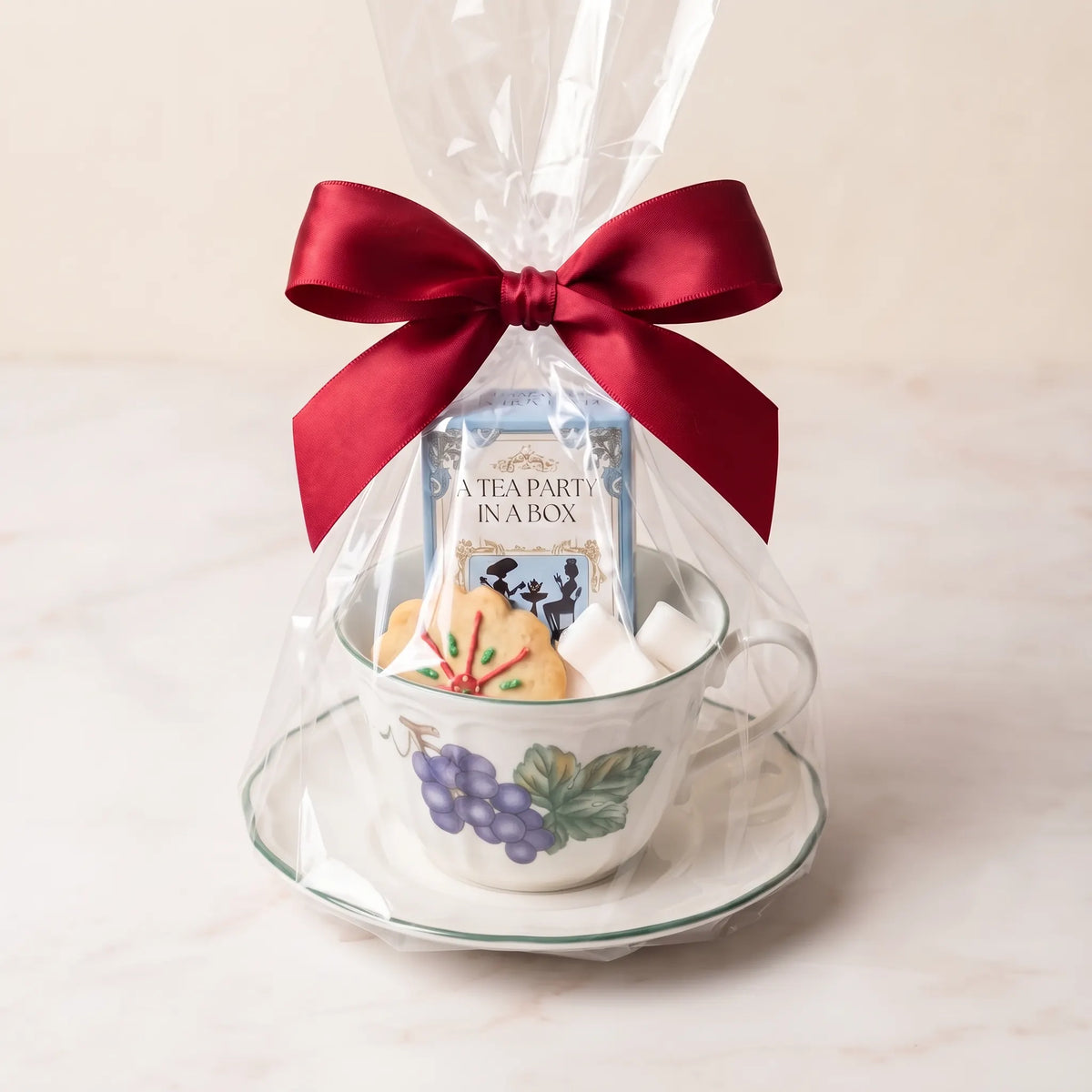 Grapevine teacup and saucer gift set in cellophane with a red bow, tea box, cookie and sugar cubes