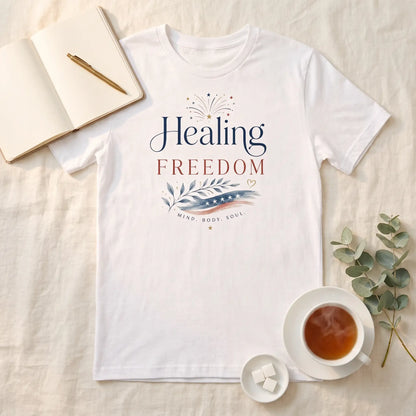 White Healing Is Freedom Fourth of July shirt laid flat beside a teacup, open journal, and eucalyptus