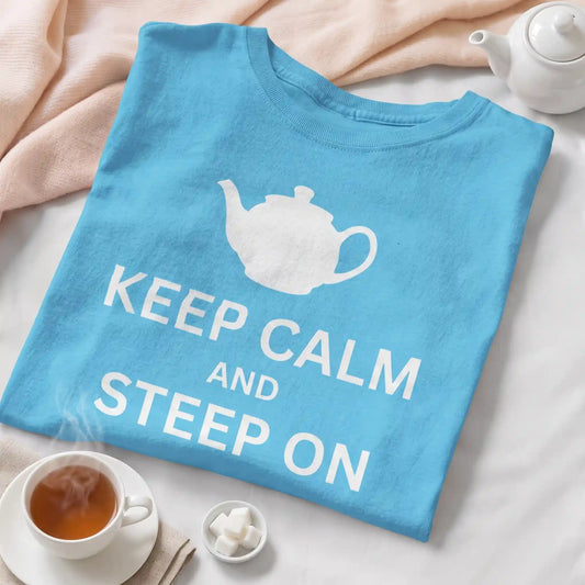 Folded turquoise Keep Calm and Steep On tea shirt with a white teapot print beside a teacup, teapot, and sugar cubes