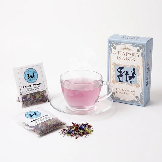 Lovely Lavender tea brewed in a clear glass teacup beside two labeled loose leaf tea sachets and the A Tea Party In A Box gift box