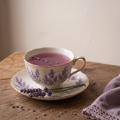 Cup of brewed Lovely Lavender tea in pink-purple with lavender buds floating and fresh sprigs beside the saucer