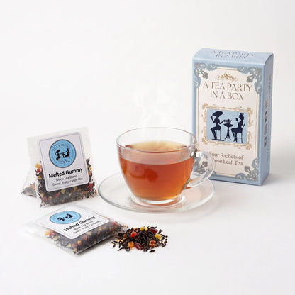 Melted Gummy tea brewed in a clear glass teacup beside two labeled loose leaf tea sachets and the A Tea Party In A Box gift box