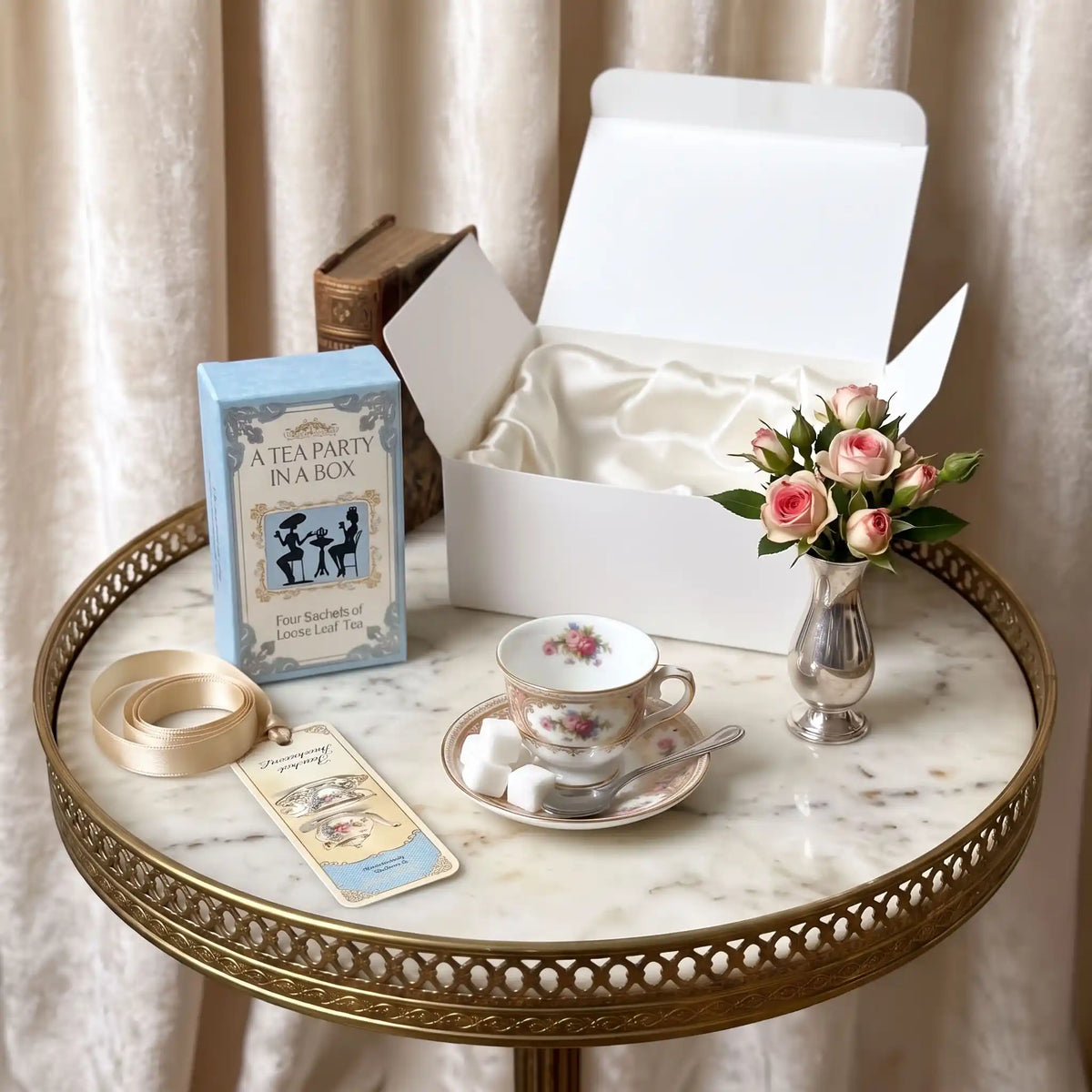 A Mini Tea Party In A Box open on a white table with a floral mini teacup, tea spoon, sugar cubes, and a blue tea box