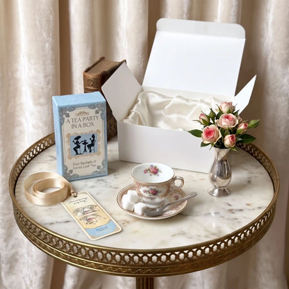 A Mini Tea Party In A Box open on a white table with a floral mini teacup, tea spoon, sugar cubes, and a blue tea box