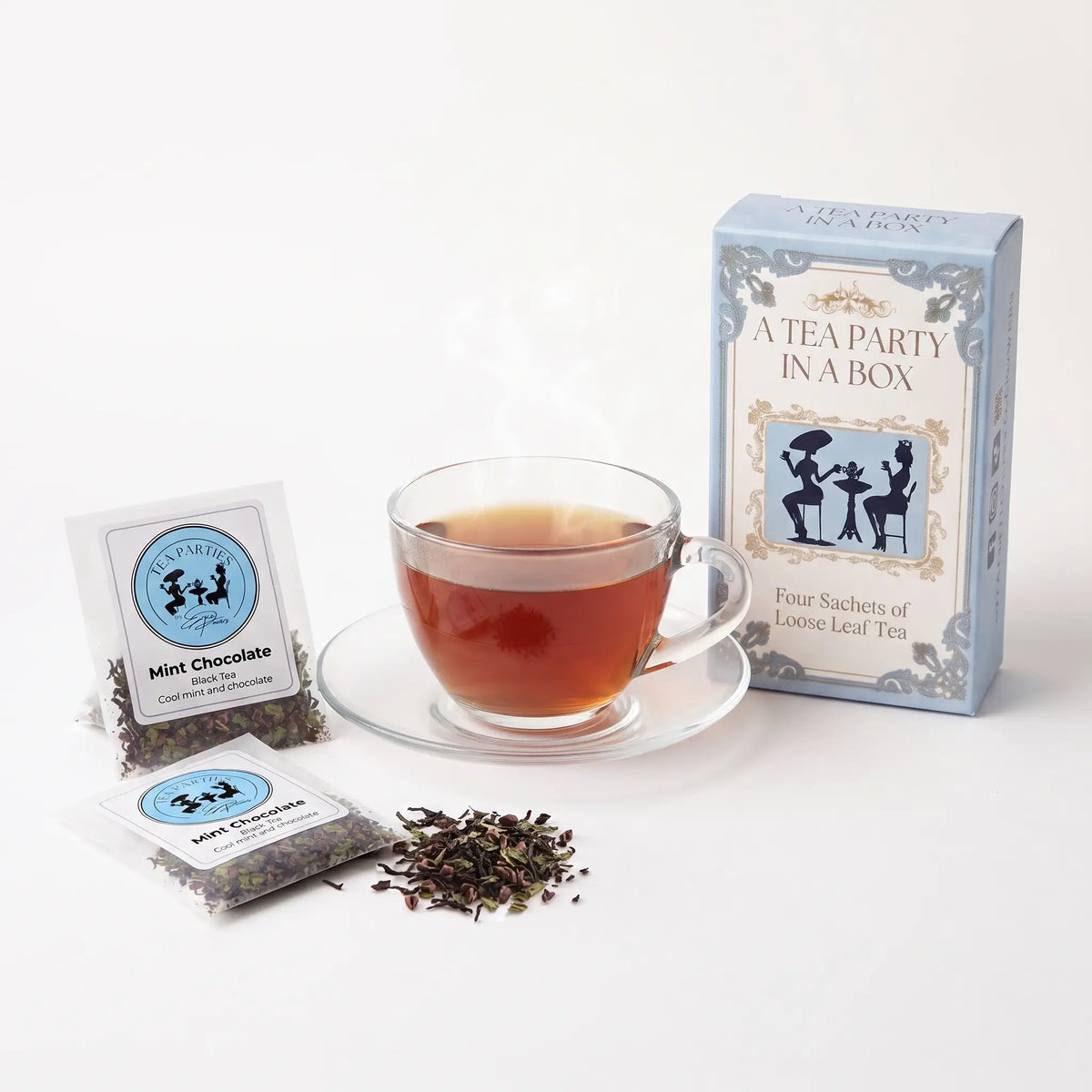 Mint Chocolate tea brewed in a clear glass teacup beside two labeled loose leaf tea sachets and the A Tea Party In A Box gift box