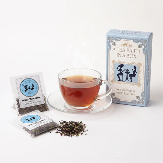 Mint Chocolate tea brewed in a clear glass teacup beside two labeled loose leaf tea sachets and the A Tea Party In A Box gift box
