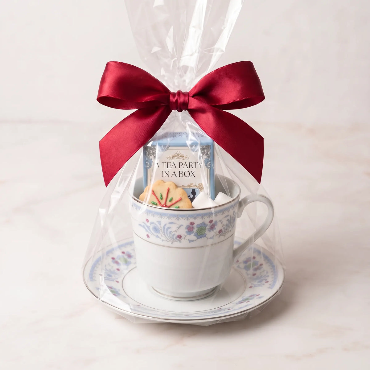 Pink Posy teacup and saucer gift set in cellophane with a red bow, tea box, cookie and sugar cubes