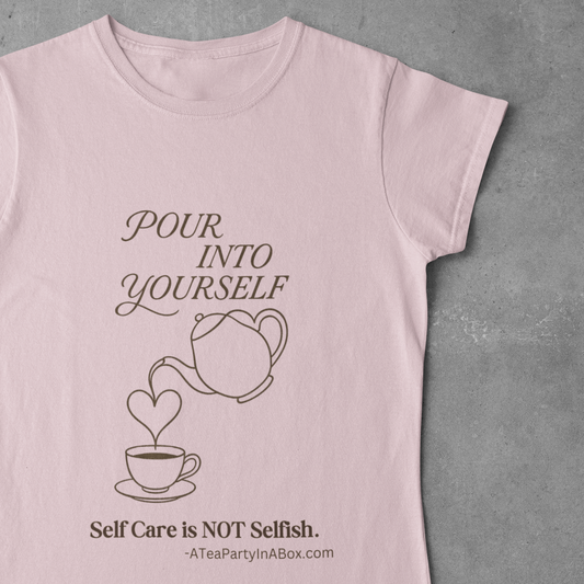 A light pink short-sleeve t-shirt with a brown graphic print of a teapot pouring into a teacup with the text 'Pour Into Yourself. Self Care is NOT Selfish.