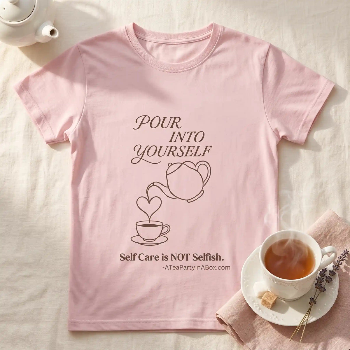 Pink Pour Into Yourself self-care tea shirt laid flat beside a steaming teacup, small teapot, and lavender