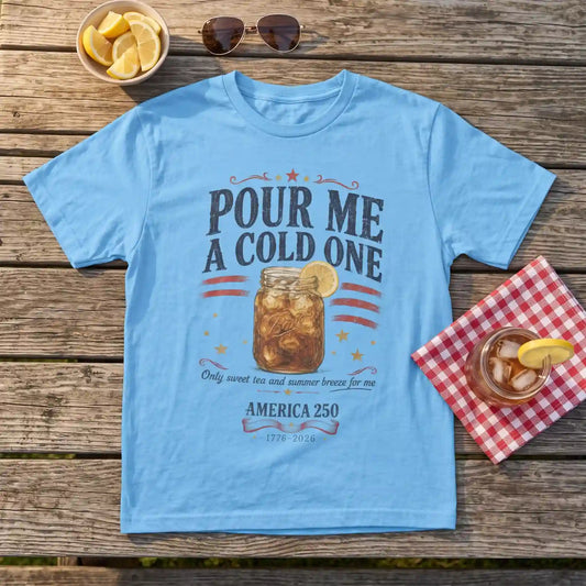 Light blue Pour Me a Cold One sweet tea shirt on a picnic table beside a mason jar of iced sweet tea with lemon