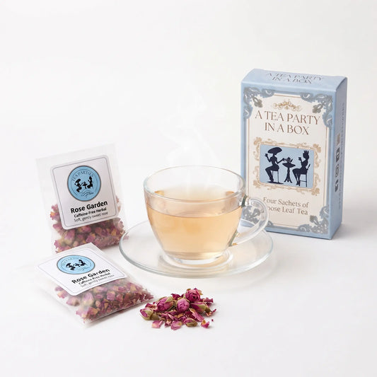 Rose Garden tea brewed in a clear glass teacup beside two labeled loose leaf tea sachets and the A Tea Party In A Box gift box
