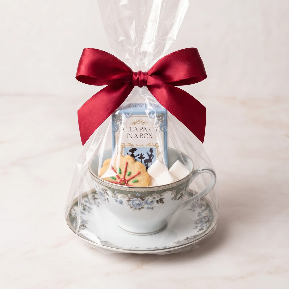 Sage Scroll teacup and saucer gift set in cellophane with a red bow, tea box, cookie and sugar cubes