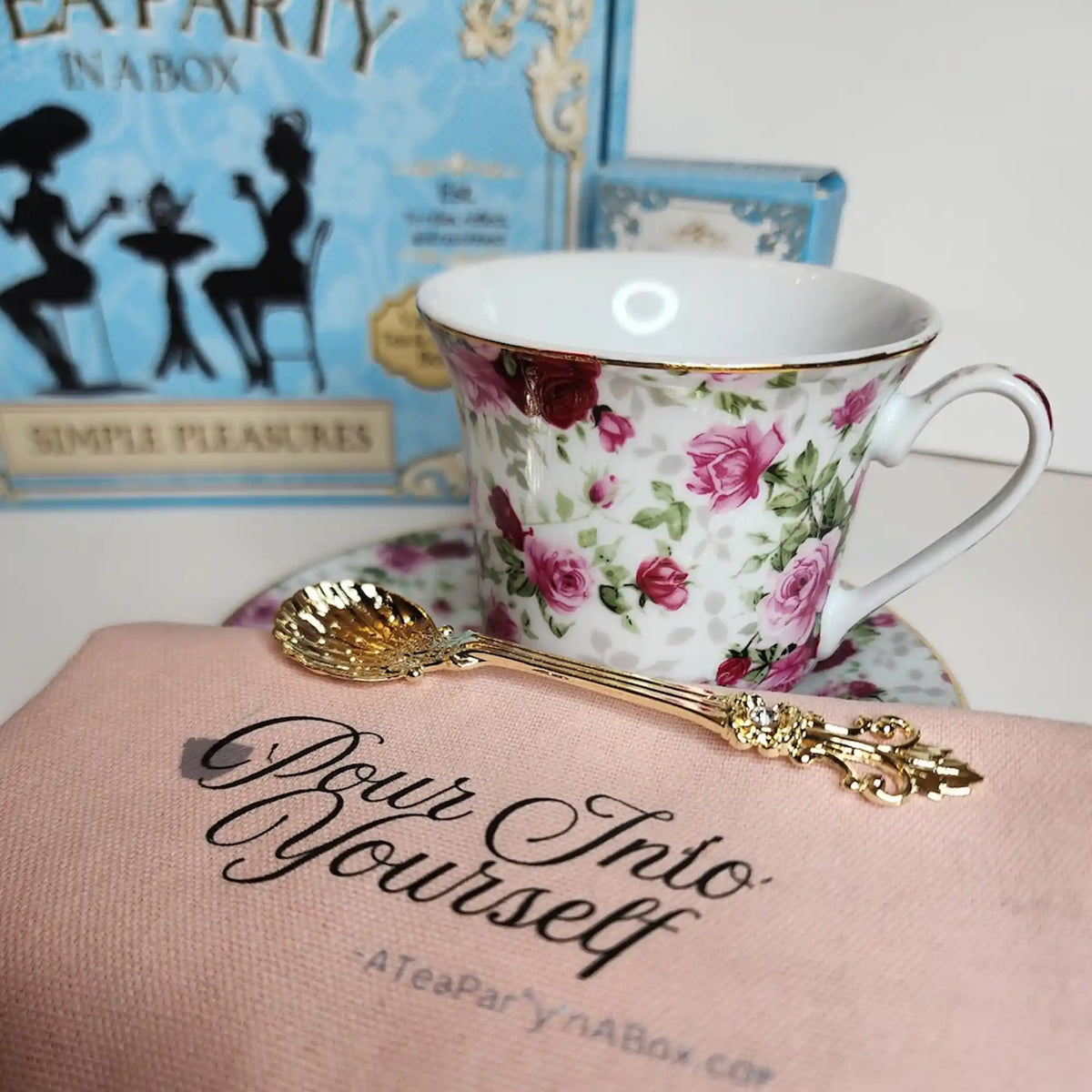 Rose teacup and saucer with a gold-tone shell teaspoon on a blush Pour Into Yourself pouch from the Simple Pleasures box