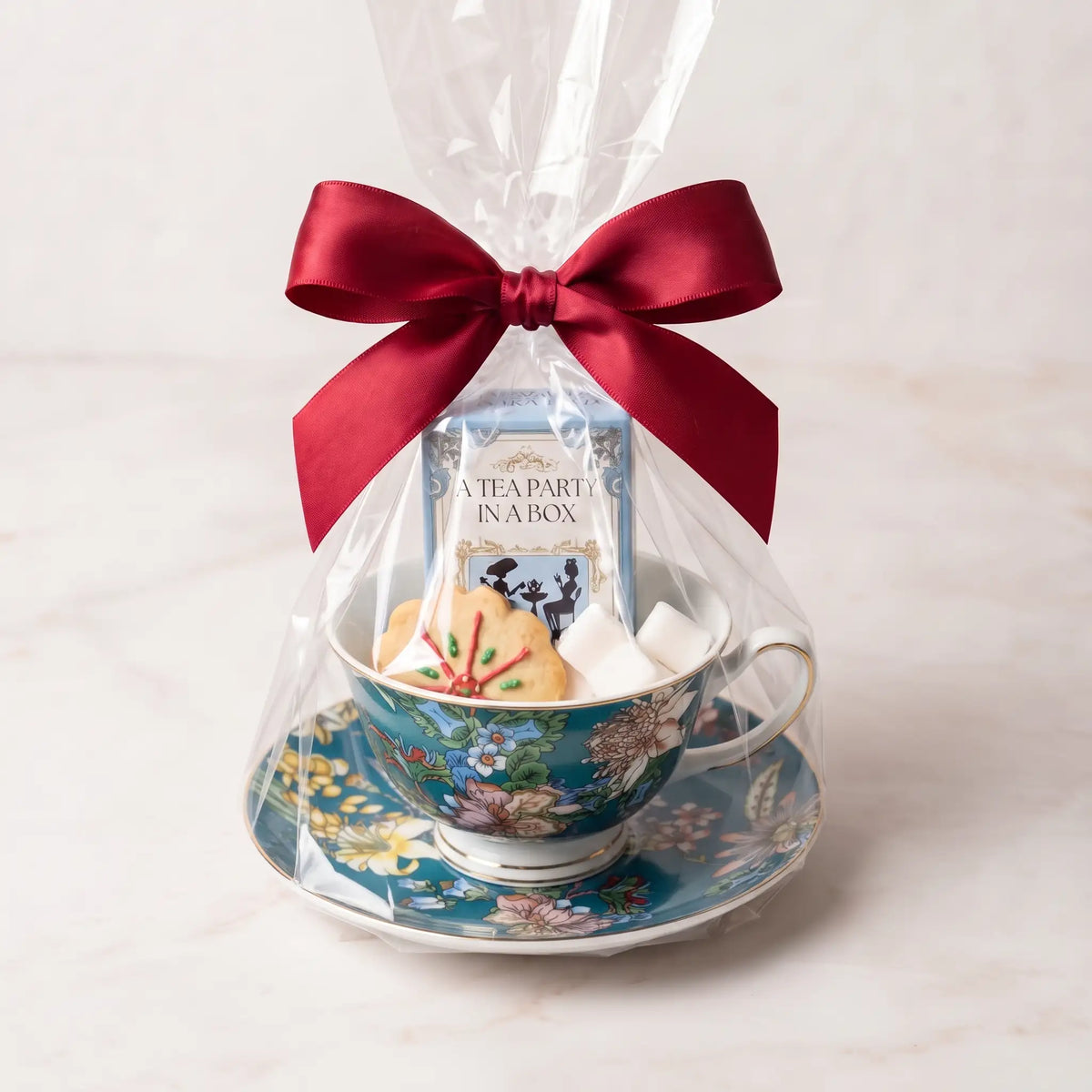 Teal Botanica teacup and saucer gift set in cellophane with a red bow, tea box, cookie and sugar cubes